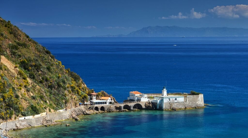 Beautiful coastal view with a fortress in Skikda, Algeria, showing vibrant blue sea and lush hills.