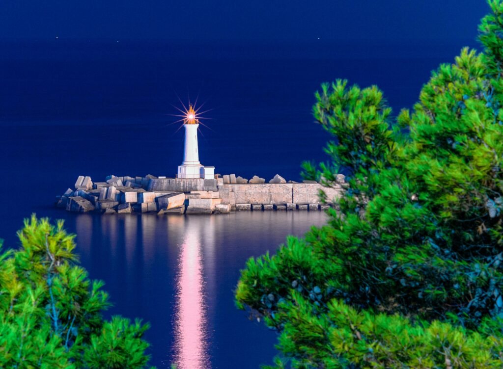 Illuminated lighthouse reflecting in the sea at twilight in Skikda, Algeria.