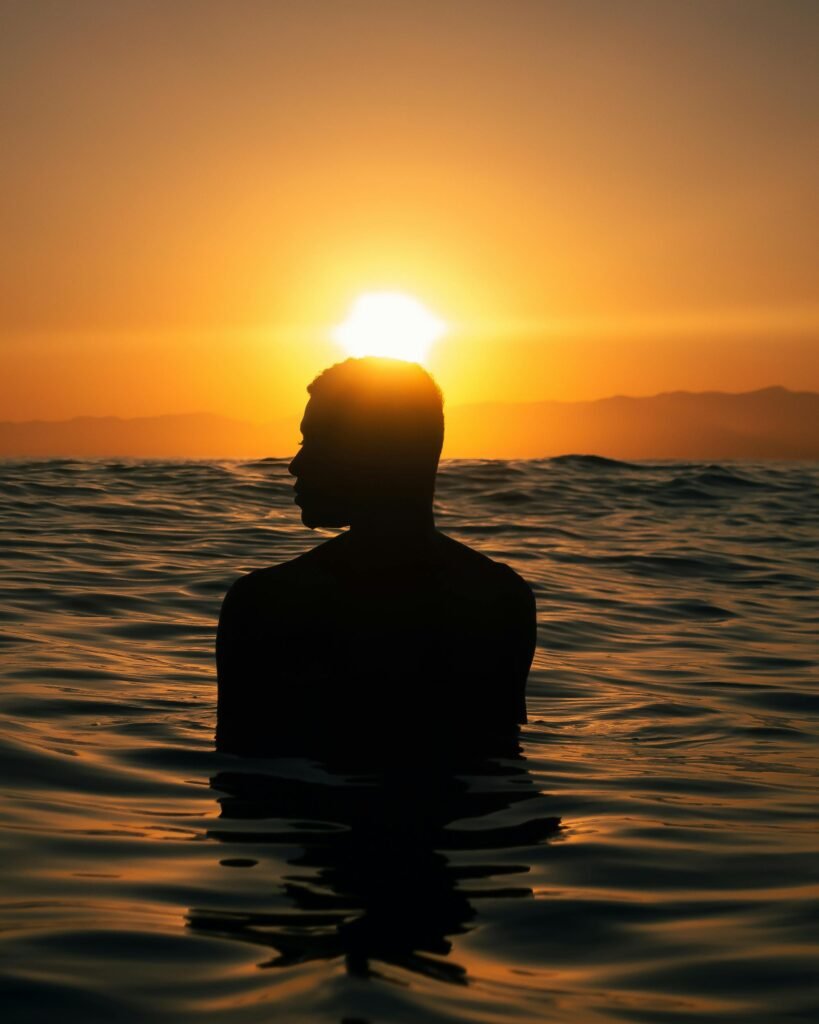 Captivating silhouette of a man standing in the ocean at sunset in Tichy, Algeria.