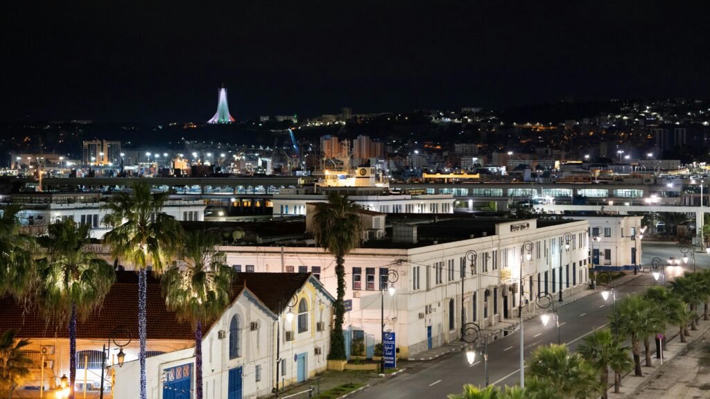 A nighttime cityscape of Alger Centre, featuring the illuminated Maqam Echahid in the background.