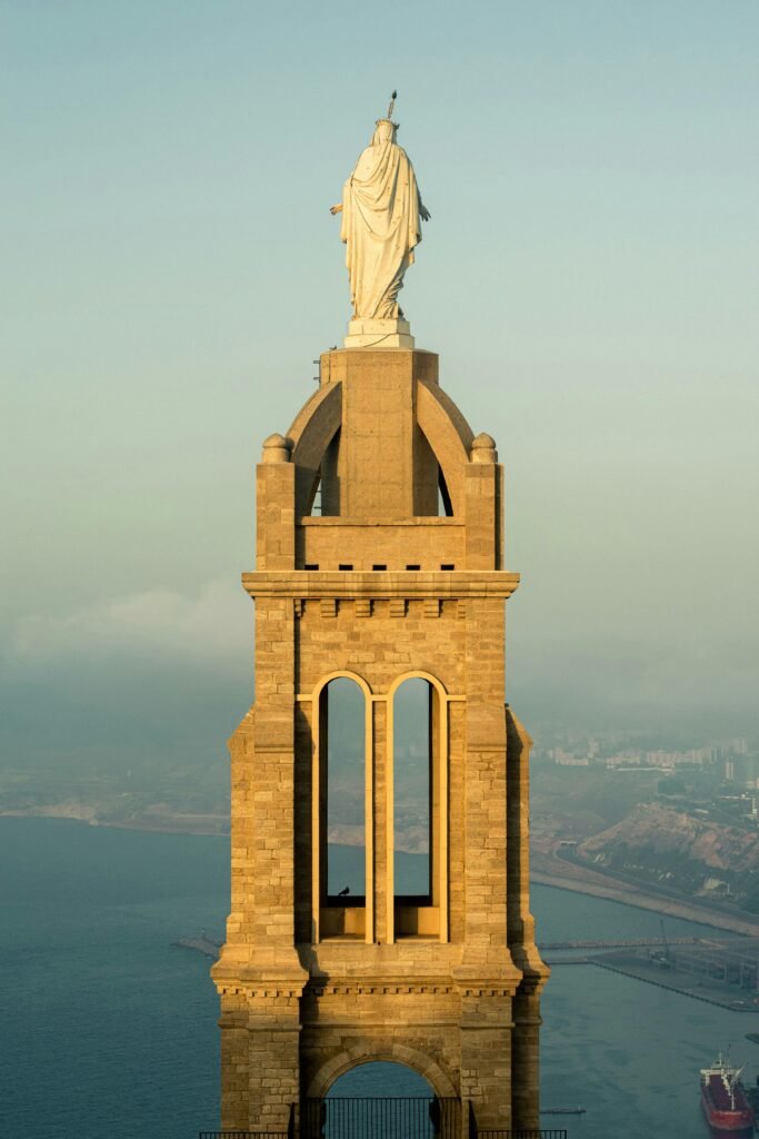 Stunning view of a statue crowning a grand tower with coastal backdrop at sunrise.