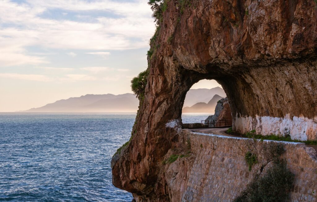 Coastal road cutting through arch rock formation with sea view in Jijel, Algeria.